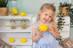 Ein Mädchen vor einem Limostand. Sie hält eine Zitrone in der Hand. Kindergartenfotograf Set modern