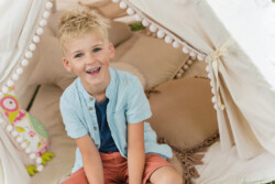 Kindergartenfotograf in Illertissen. Eine Junge sitzt im Schneidersitz in einem Zelt und lacht in die Kamera