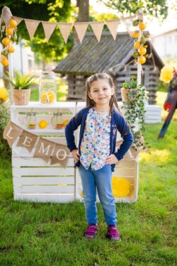 Kindergartenfotograf macht draußen Fotos im Garten. Ein Mädchen mit Händen in den Hüften