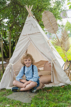 Kindergartenfotograf für Memmingen. Ein Junge sitzt im Schneidersitz und Hosenträgern vor einem Boho-Zelt