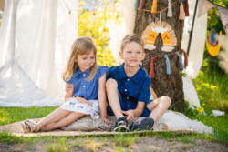 Kindergartenfotograf in Ulm. Geschwisterfoto. Ein Junge und ein Mädchen sitzen auf einem Teppich. Ein Baum mit Dekoelementen im Hintergrund