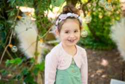 Kitafotograf für Krumbach. Ein Mädchen steht im Kindergarten draußen im Garten und lacht in die Kamera