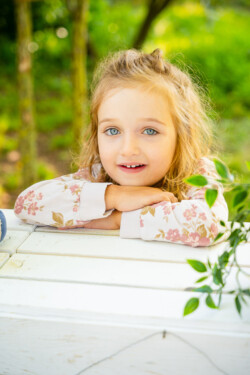 Kindergartenfotograf Günzburg. Ein Mädchen lehnt sich auf weisse Kisten und schaut in die Kamera