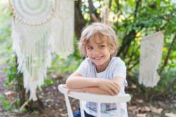 Kindergartenfotograf Neu-Ulm. Ein Junge mit blonden Haaren sitzt lächelnd auf einem umgedrehten Stuhl