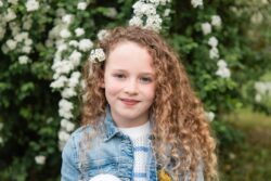 Mädchen mit lockigen Haaren beim Kita-Shooting vor weissen Blumen