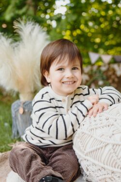 Kinderfotografie im Kiga. Kleiner Junge mit schwarz weissem Pulli lehnt sich auf ein großes Kissen mit weissen Büschelgras im Hintergrund