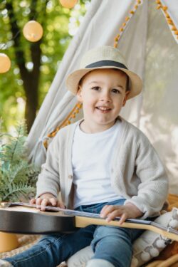 Junge mit Hut sitzt in einem Zelt und spielt Ukulele. Kindergartenbilder bei Ulm